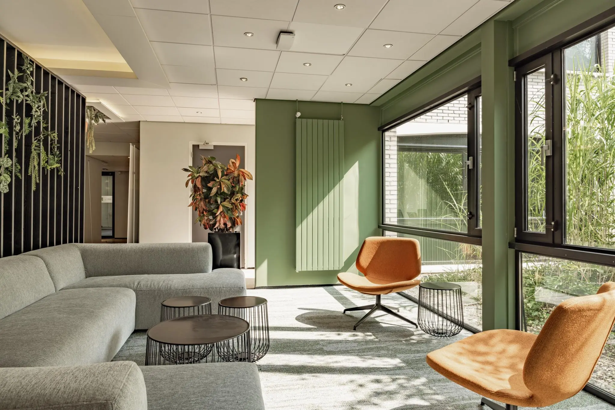 Moderne wachtruimte in het gemeentehuis aan de Burgemeester Verderlaan met groene muren, oranje stoelen en grote ramen.